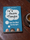A paperback copy of a book titled "It's Just a Thought: Tame your mind, Free your spirit" on a wooden table next to a cup of coffee.